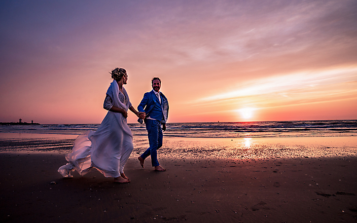 Bruid en Bruidegom wandelen Scheveningen strand zonsondergang oranje paarse lucht Bruidsfotograaf Stefan van Beek