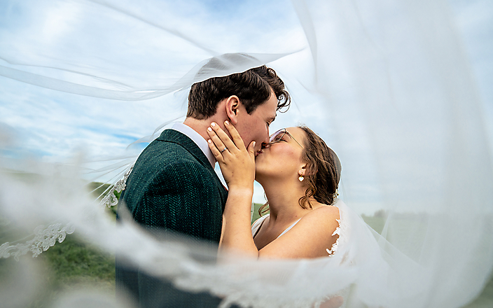 Kussend bruidspaar tussen sluier van bruid – Trouwfotograaf Stefan van Beek